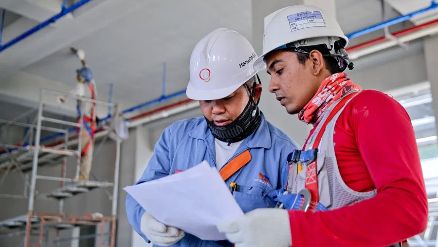 Two workers, with hard hats and protective gear, in a factory environment