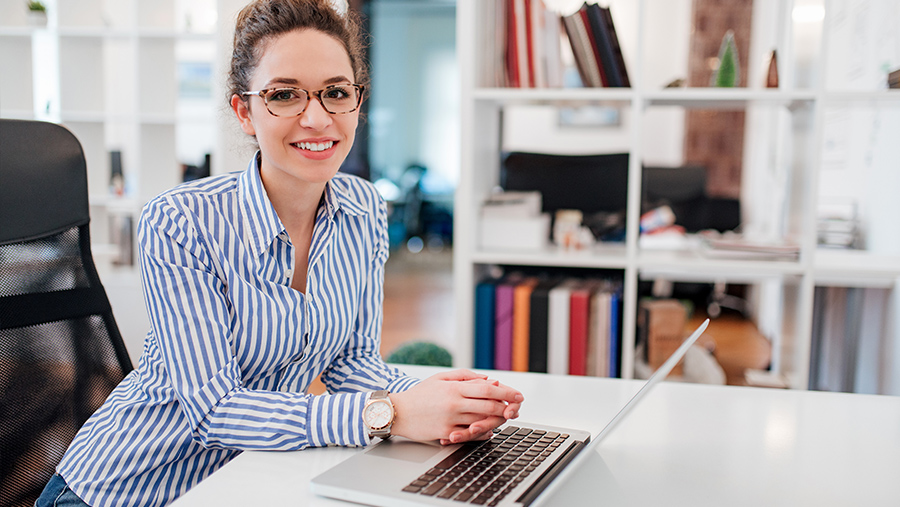 A professional looking woman, happy, with a laptop in her desk